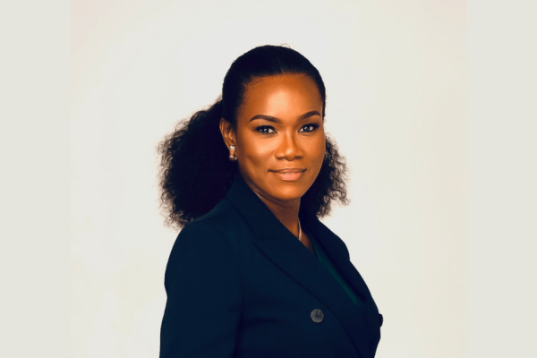 A portrait of a smiling Ivy Heward-Mills. Ivy is a Black woman wearing a dark top with tied back shoulder length hair